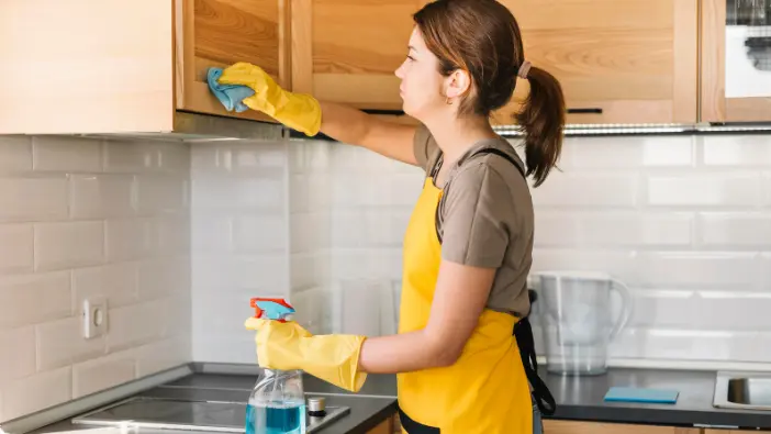 A woman in a yellow apron is engaged in cleaning tasks within a kitchen, emphasizing her dedication to cleanliness.