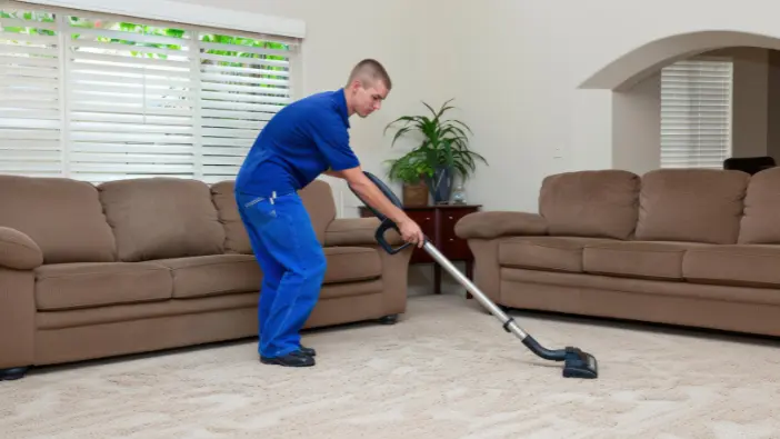 A man using a vacuum cleaner to clean a room, focusing on maintaining a tidy and dust-free environment.