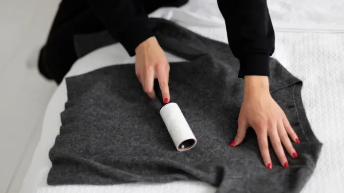 A woman rolls a sweater on a bed, demonstrating an efficient method of clothing organization.