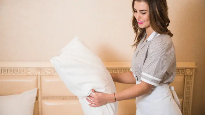 A young woman dressed in a uniform holds a pillow, exuding a sense of readiness and professionalism in her posture.