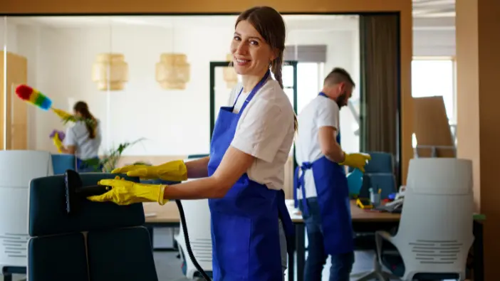 A woman dressed in an apron is actively cleaning a chair, emphasizing her role in upkeeping a neat living space.