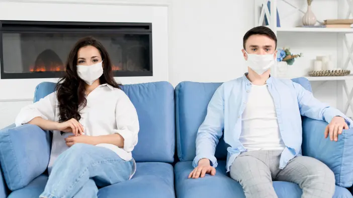 A masked couple sits on a couch, reflecting a sense of unity and care while navigating health precautions.