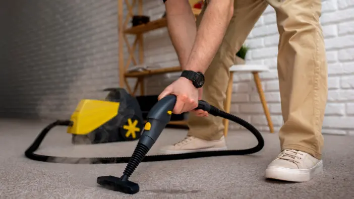 A man using a vacuum cleaner to clean a carpet, demonstrating effective home maintenance and cleanliness.