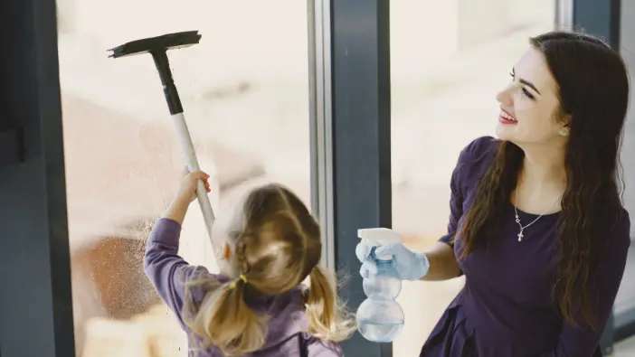 A woman and a little girl working side by side to clean windows, highlighting their collaborative effort and shared activity.