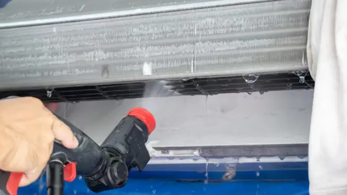 A person is seen using a hose to clean a AC Coils, demonstrating an efficient method for maintaining cleanliness.